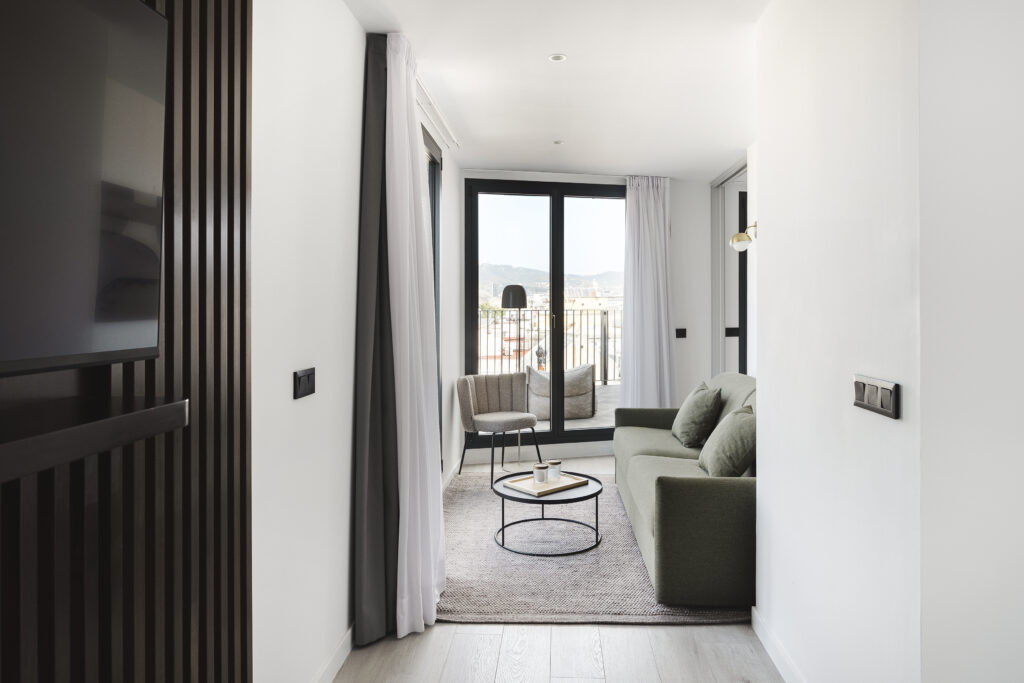 Bright living room at master La Rambla Barcelona with green sofa, round coffee table, and access to a spacious terrace with city views.