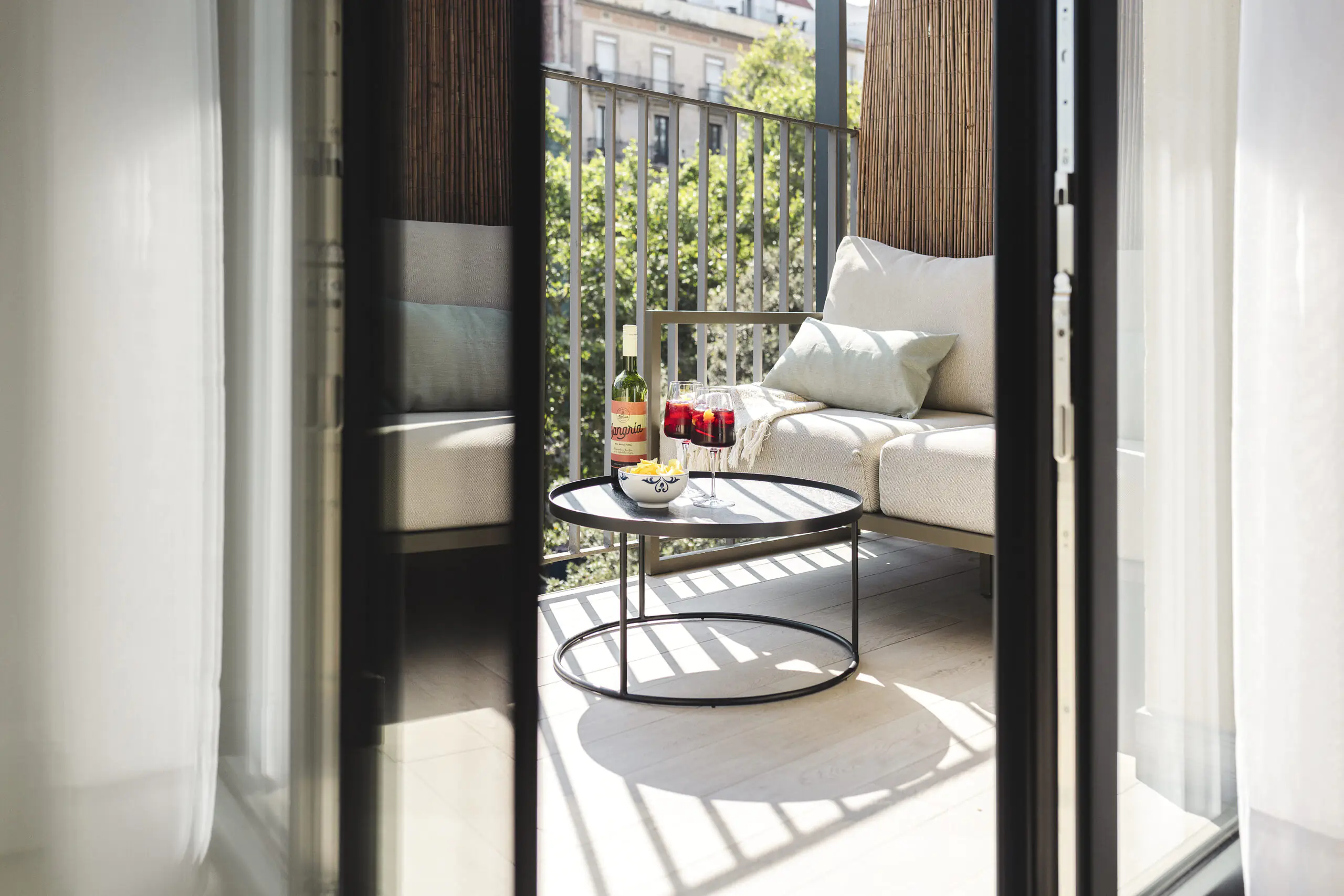 Private balcony at master La Rambla Barcelona with a cozy lounge sofa, round table, and sangria glasses overlooking the city.